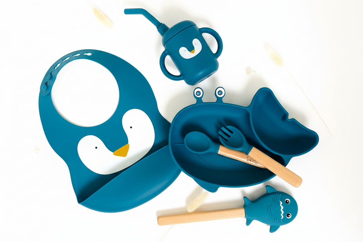 Blue children's dining set with bib, cup, plate, and utensils on a white background