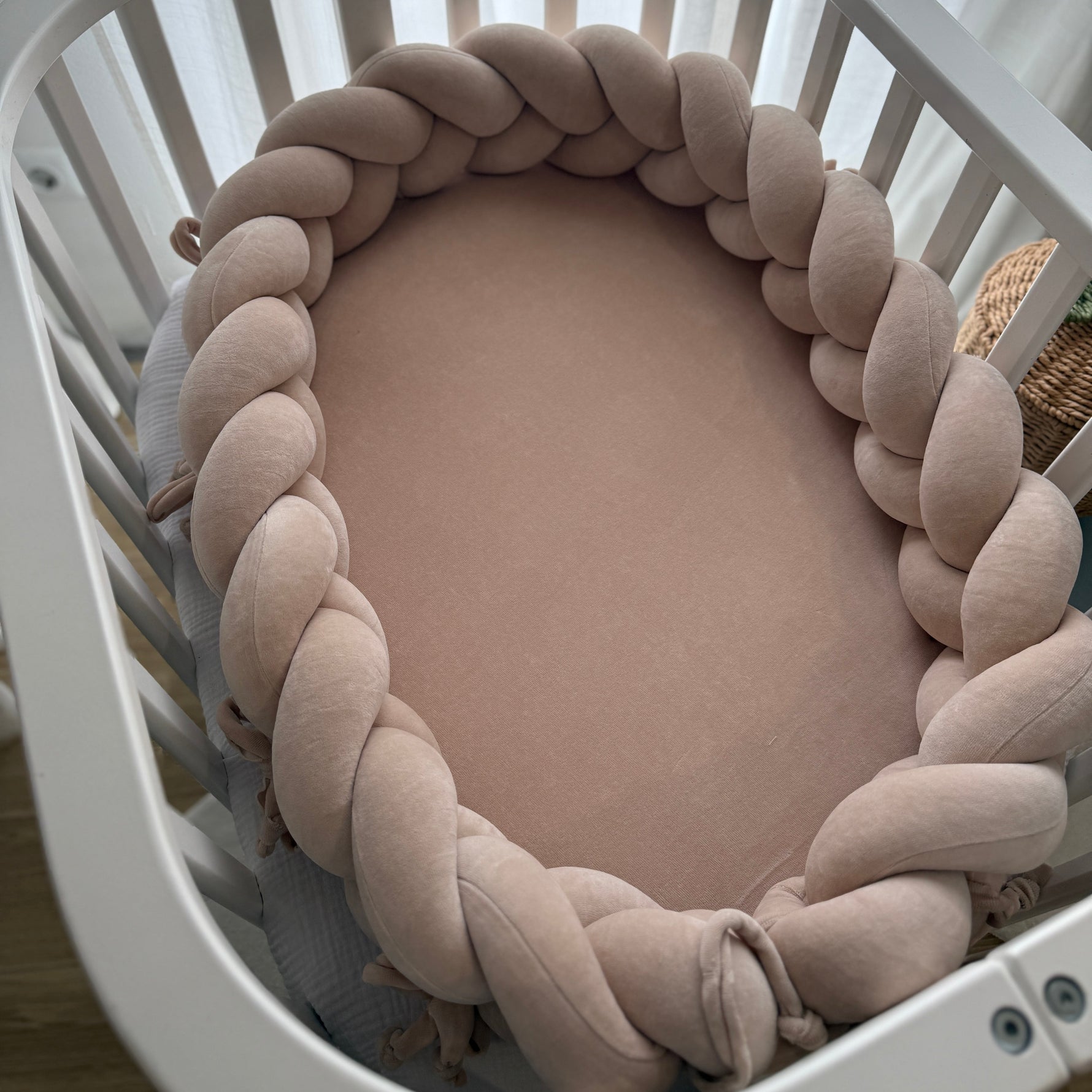 Baby crib with a braided beige bumper pad inside