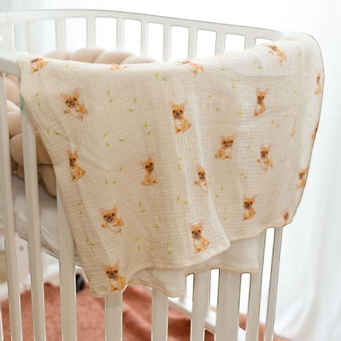 Baby Natur muslin swaddle blanket with French bulldog print and green leaves on a cream background.