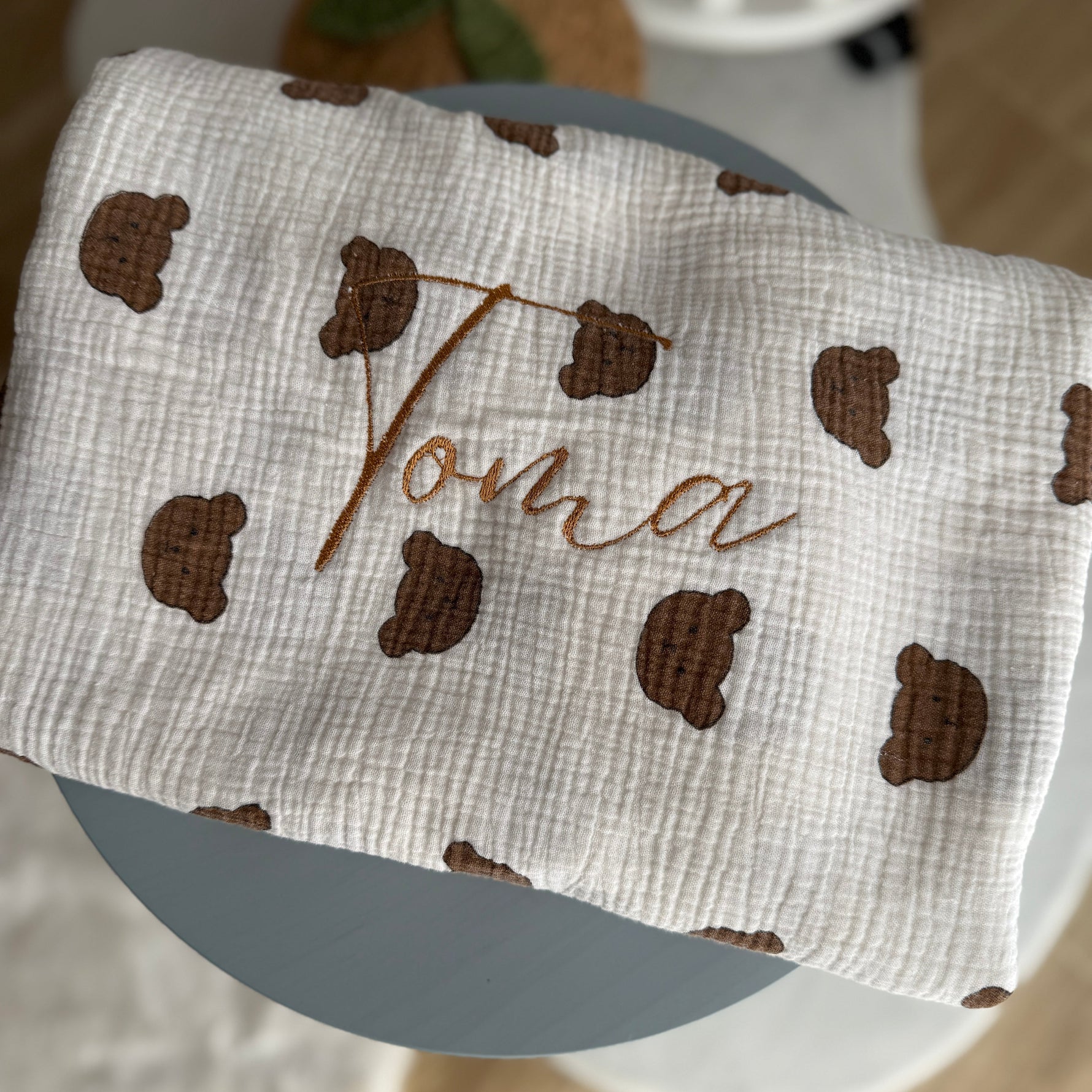 Baby blanket with brown leaf patterns and embroidered name on a chair.