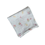 Baby Natur white cotton muslin swaddle blanket with a delicate floral print of pink and purple flowers and yellow accents.