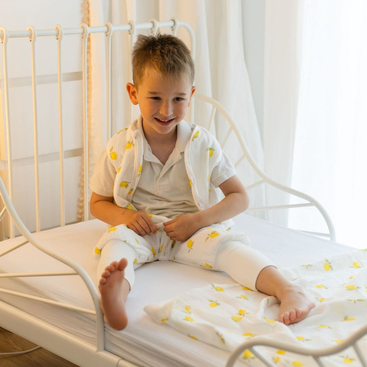 Baby Natur white muslin sleep sack with lemon print, featuring a young boy sitting on a bed.