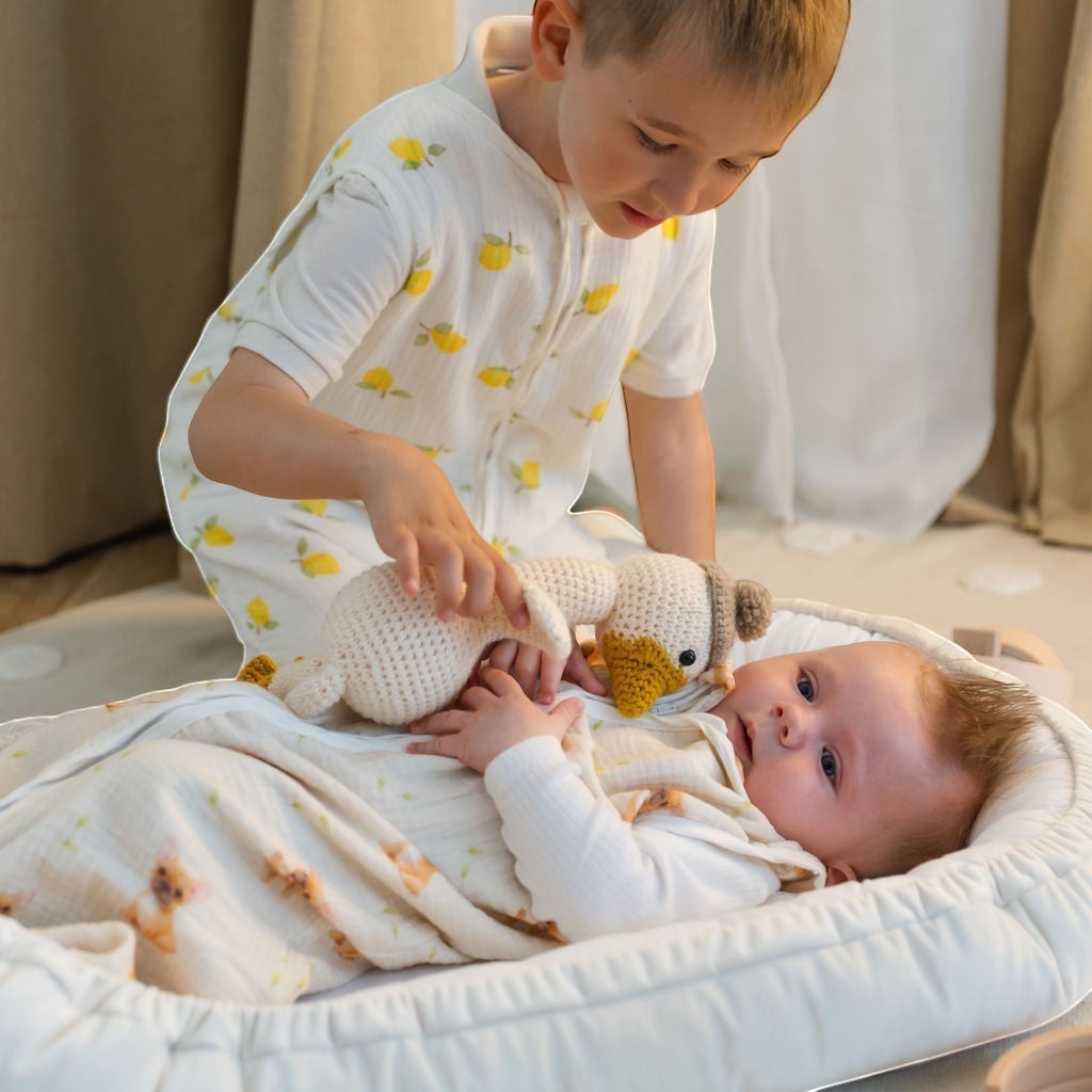 Baby Natur white sleeveless sleeping bag with yellow lemon print, worn by a boy interacting with a baby.