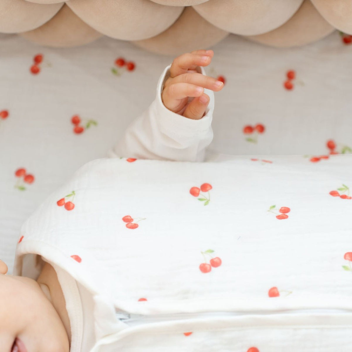 Baby Natur white cotton crib sheet with a cherry print, featuring a baby's arm.