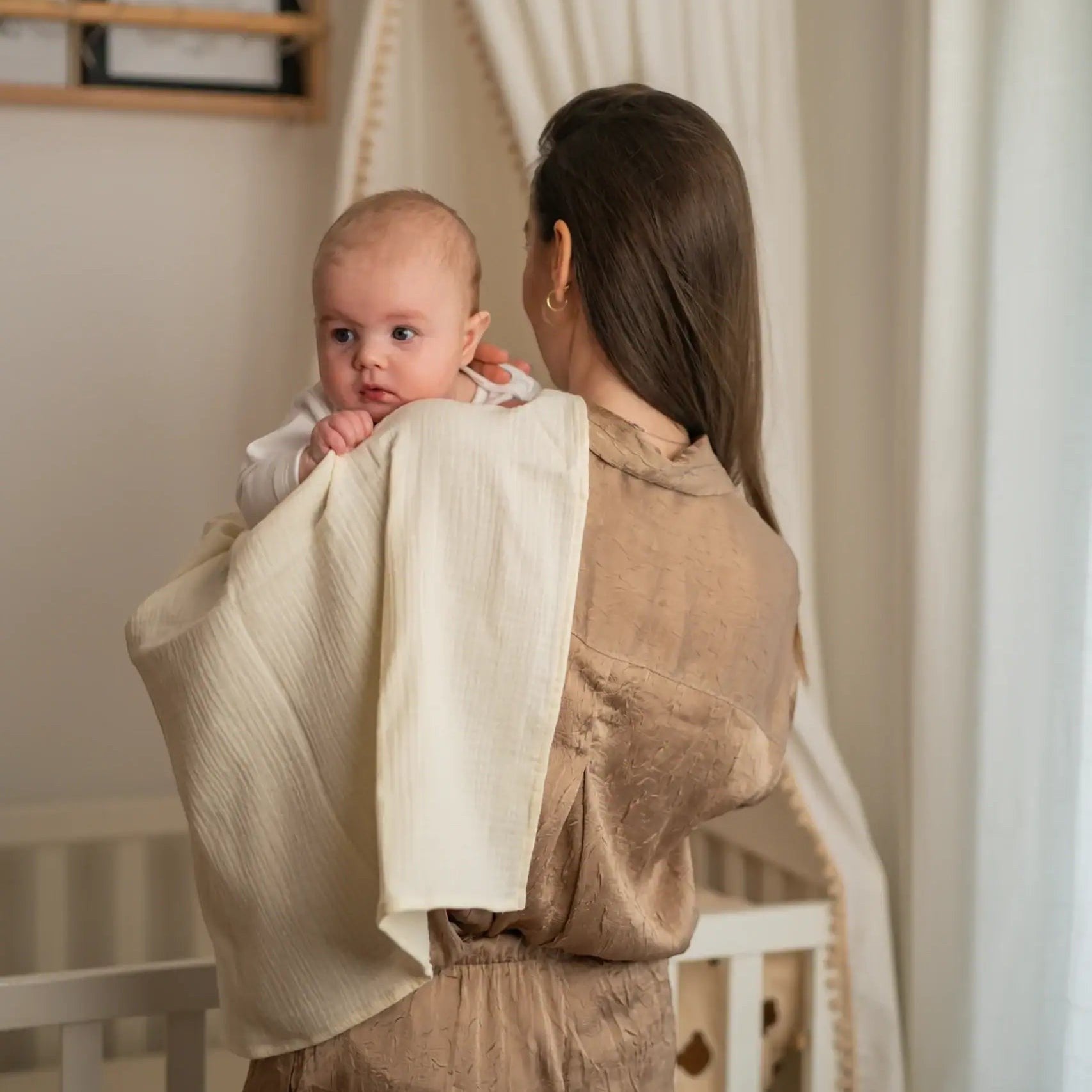 Baby NaturA cream 100% cotton muslin tetra diaper draped over a woman's shoulder holding a baby.