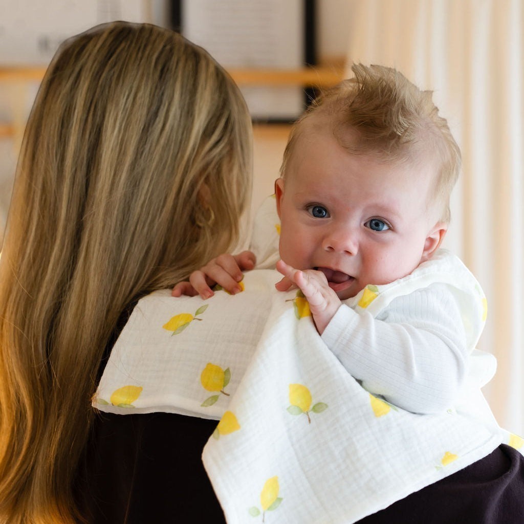 Baby Natur white cotton burp cloth with yellow lemons, draped over a person's shoulder holding a baby.